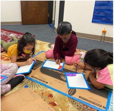 Three young learners drawing and writing together on the floor during a Little Learners activity